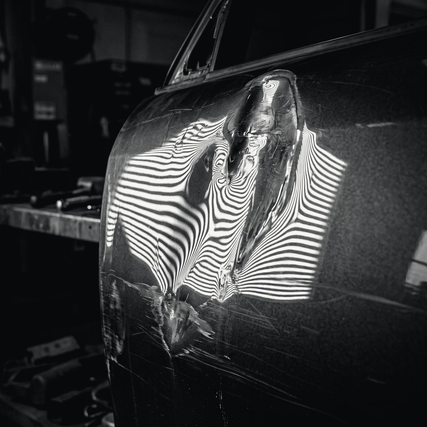 A dent in a door panel revealed by a striped inspection light