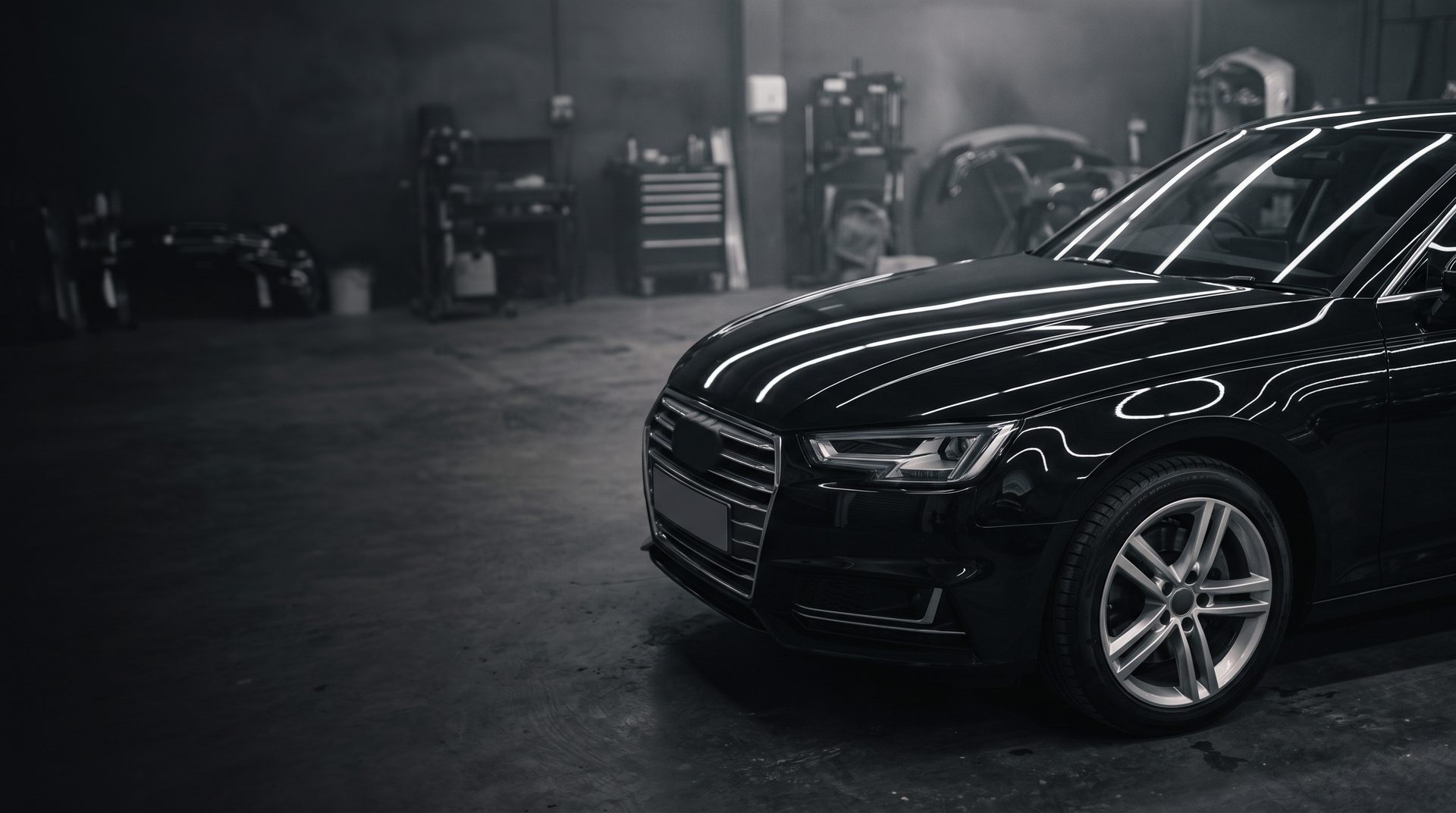 A black saloon with freshly repaired, polished bodywork under workshop strip lights